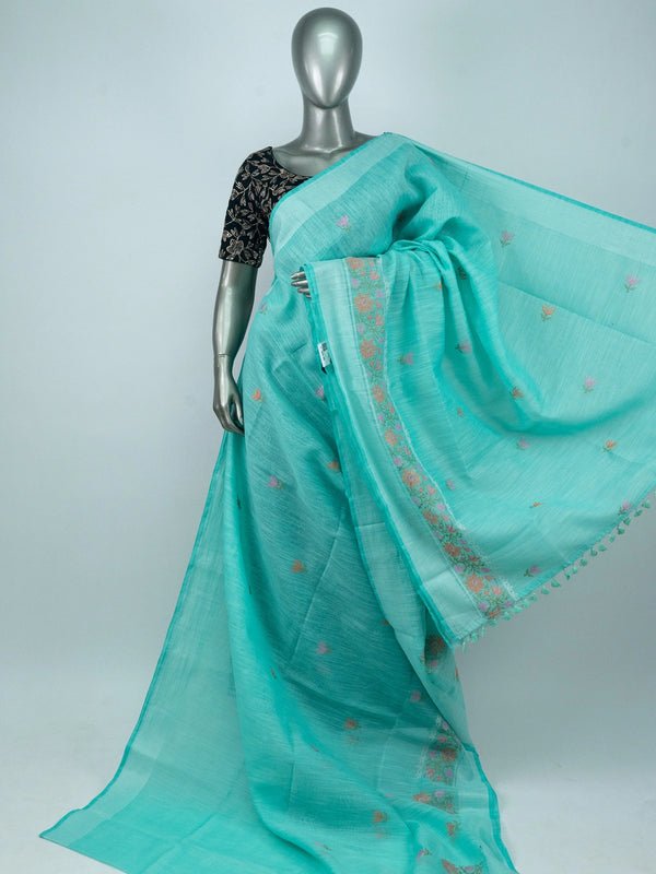 Turquoise linen cotton saree with silver zari border, floral embroidered buta and embroidered pallu, styled with a black blouse