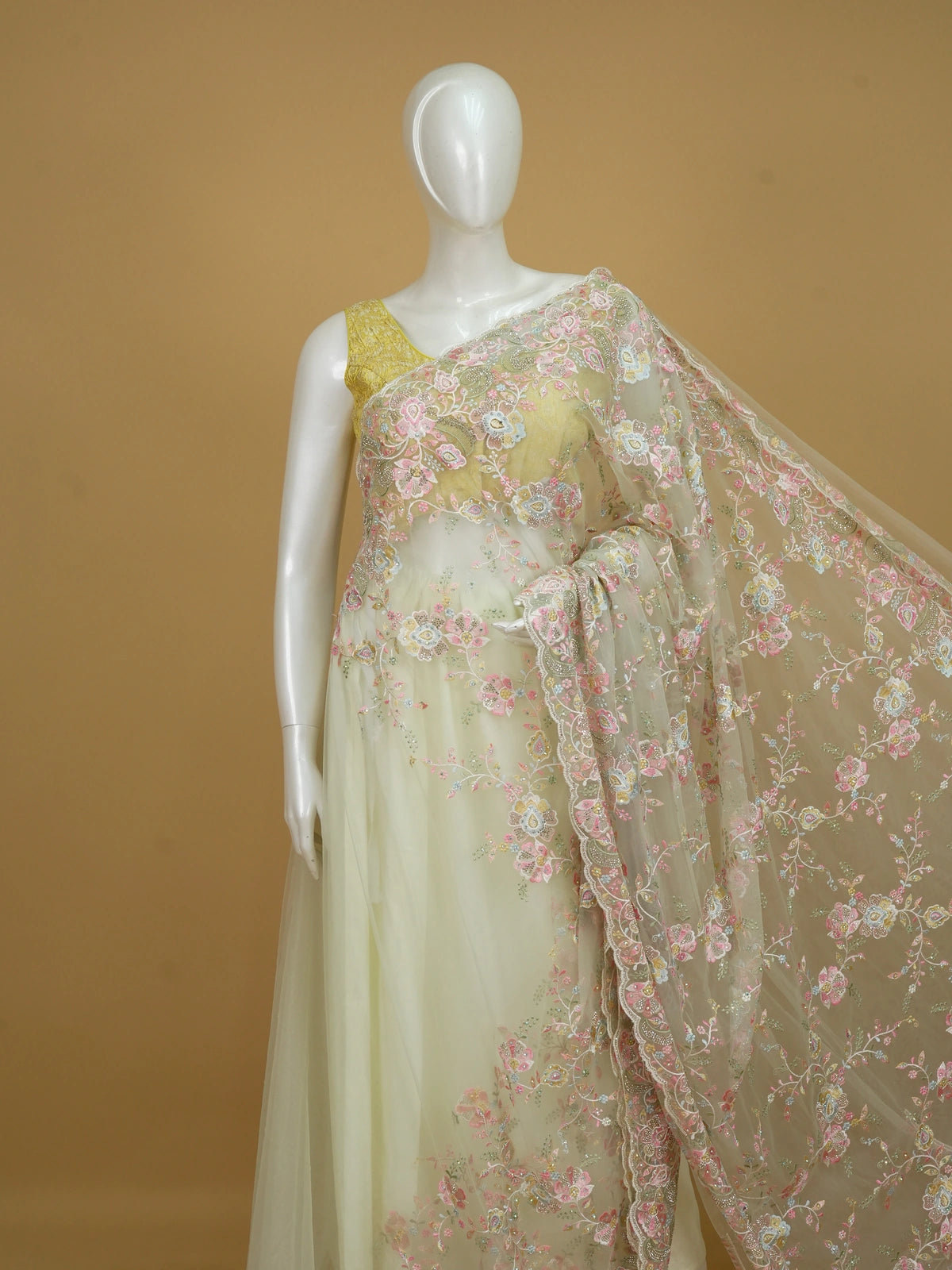 Cream net designer saree with pastel multicolour floral embroidery and scalloped border