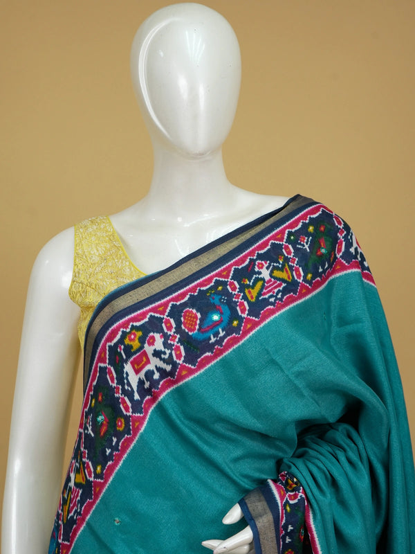 Teal linen cotton saree with navy and pink patola-style border, peacock and elephant motifs, and contrast blouse
