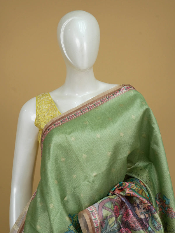 Green semi tussar saree with gold zari border, zari buttas and a multicolour Kalamkari printed pallu with a copper brown floral blouse