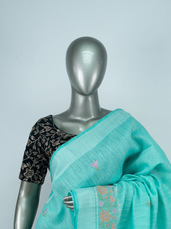 Turquoise linen cotton saree with silver zari border, floral embroidered buta and embroidered pallu, styled with a black blouse