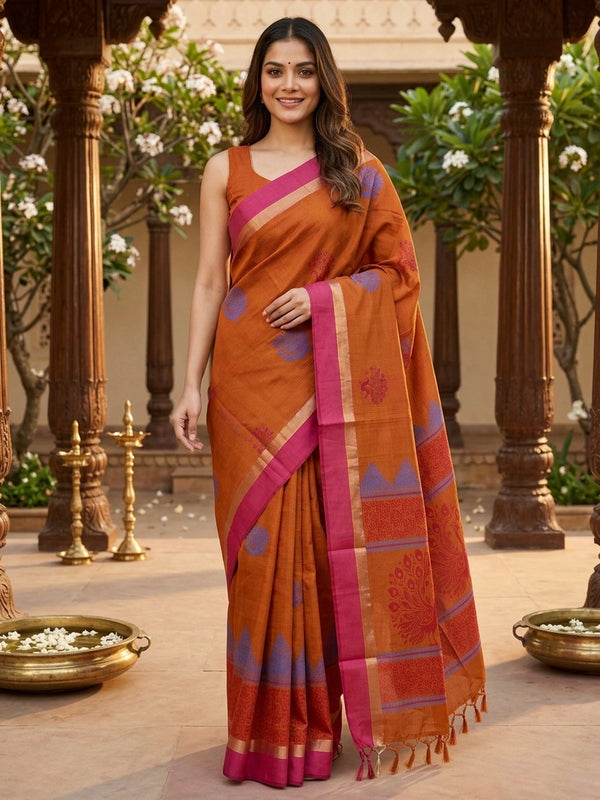 Rust orange silk cotton saree with pink zari border and blue and red peacock motifs